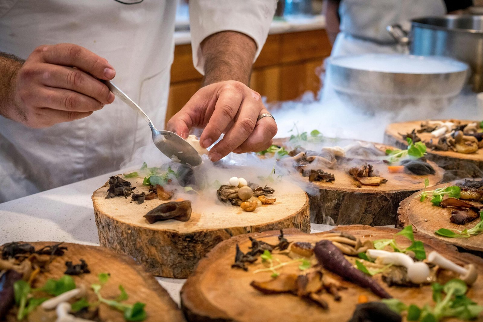 A chef artfully plating a gourmet dish with mushrooms and greens on wood slices.