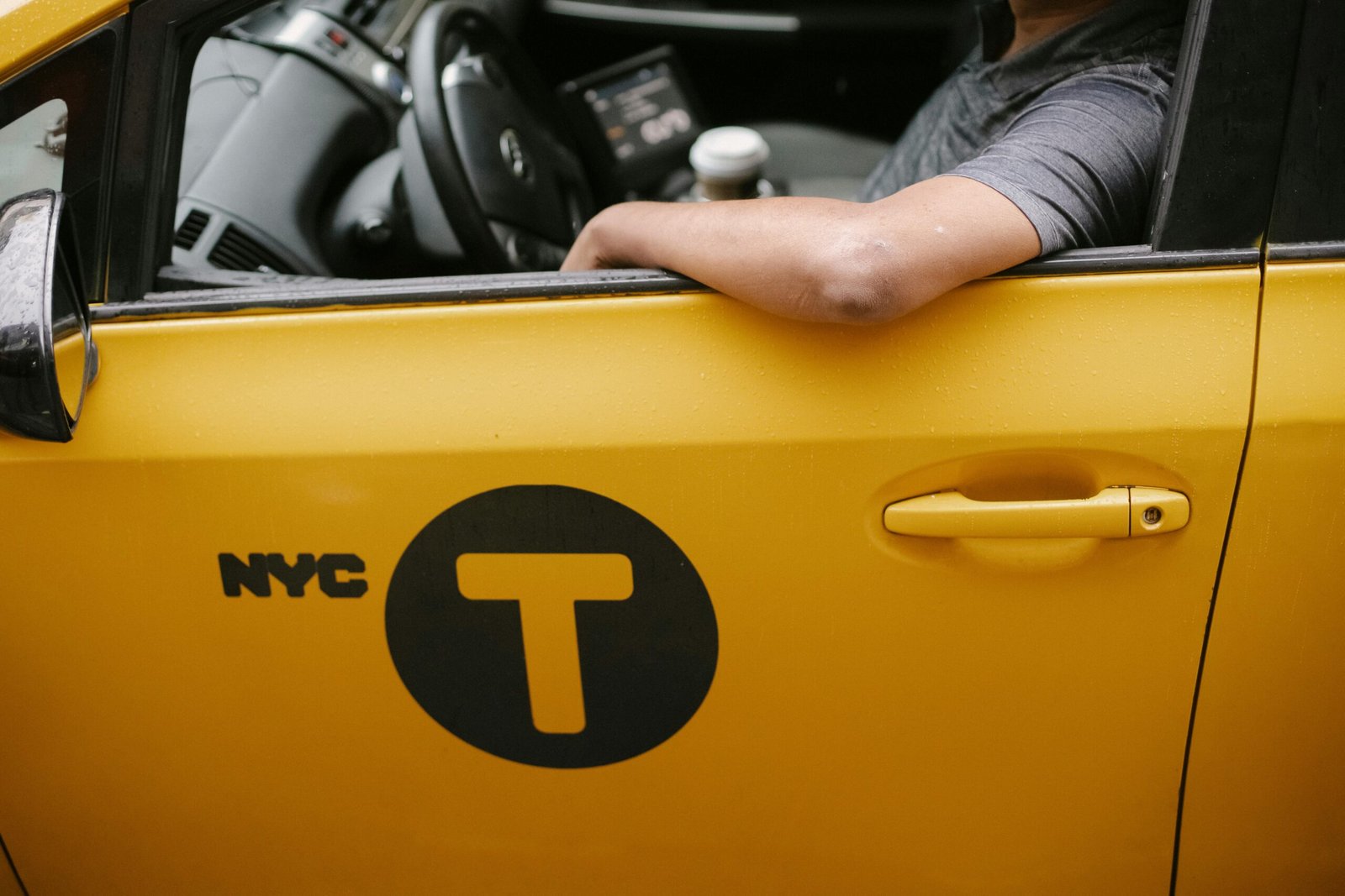 A close-up view of a yellow NYC taxi with a driver resting an arm on the window, showcasing urban transportation.