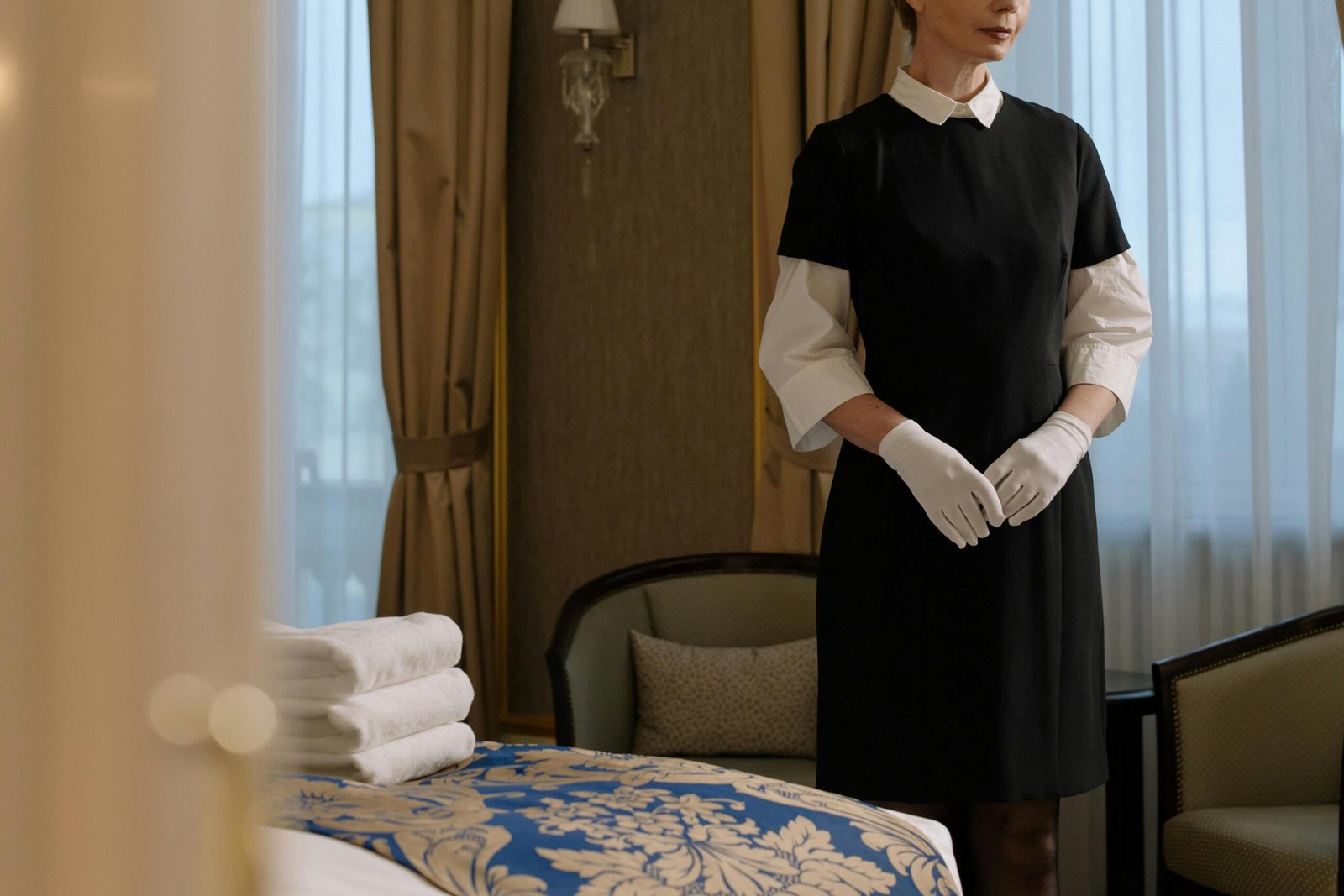 A housekeeper in uniform prepares a luxury hotel room, showcasing professionalism and service.